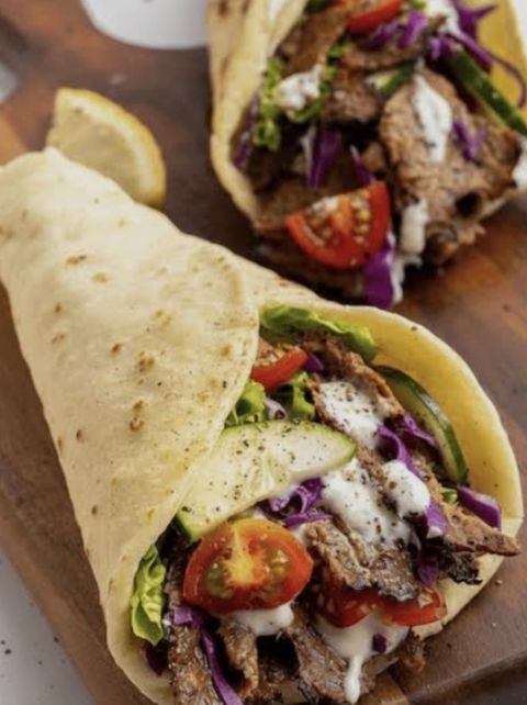 Opengesneden döner-wrap met vlees, tomaat en saus op een plank